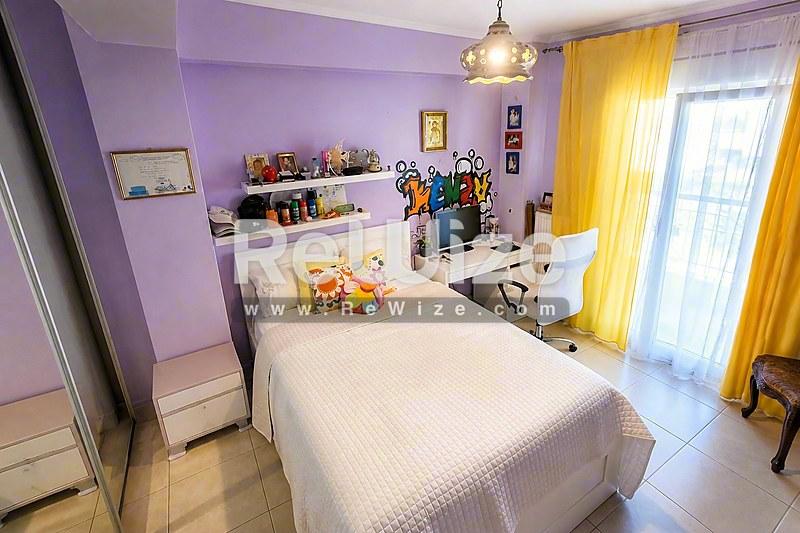 Φωτεινό υπνοδωμάτιο σε μονοκατοικία στη Χαλκιδική με λευκό κρεβάτι, μώβ τοίχους και κίτρινες κουρτίνες.
