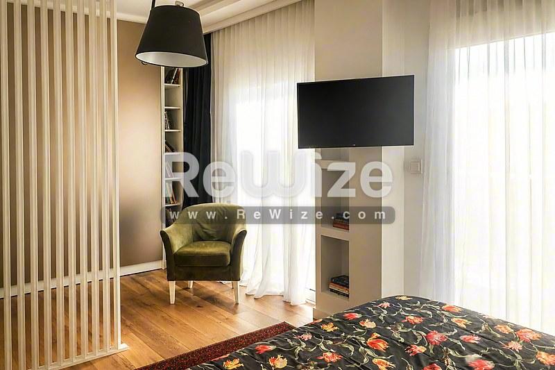 Σύγχρονη κρεβατοκάμαρα διαμερίσματος στη Χαλκιδική με λουλουδάτο κρεβάτι, πολυθρόνα και ξύλινο δάπεδο.