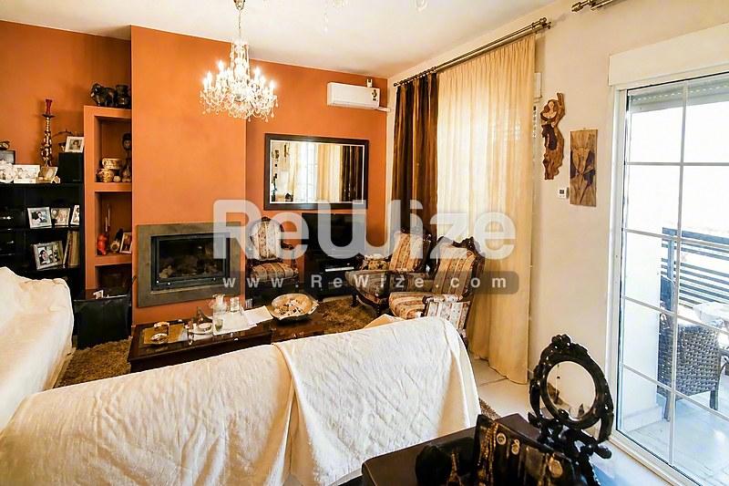 Φωτεινό σαλόνι μεζονέτας στη Χαλκιδική με πορτοκαλί τοίχους, τζάκι και σύγχρονα έπιπλα.