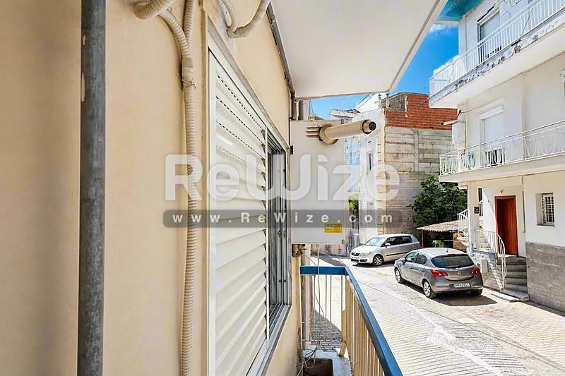 Διαμέρισμα στη Χαλκιδική με παντζούρια και θέα σε ηλιόλουστο μεσογειακό δρόμο με παρκαρισμένα αυτοκίνητα.