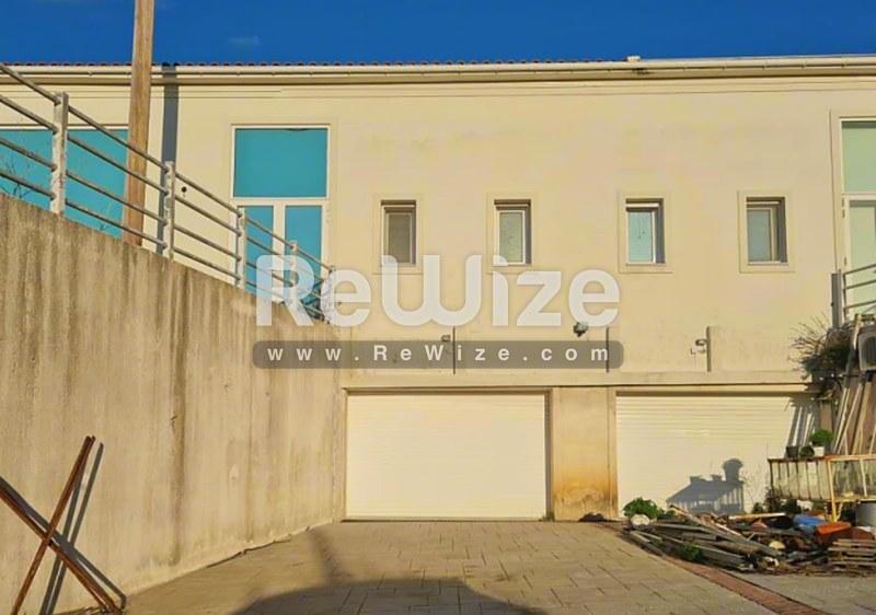 Σύγχρονη πρόσοψη καταστήματος με τσιμεντένια είσοδο στη Χαλκιδική, με πόρτα γκαράζ και κατοικία στον όροφο.