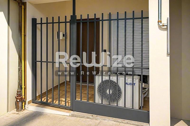 Σύγχρονη είσοδος διαμερίσματος στη Χαλκιδική με κομψή μαύρη μεταλλική πύλη και κλιματιστικό.