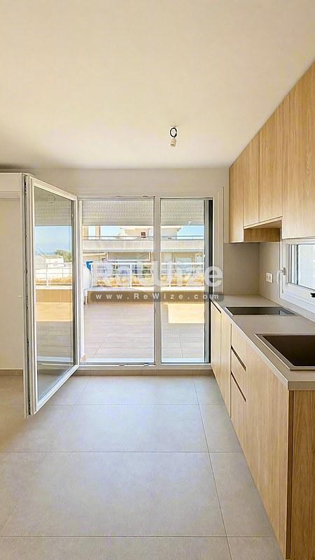 Σύγχρονη κουζίνα σε μεζονέτα της Χαλκιδικής με ξύλινα έπιπλα, σύγχρονες συσκευές και άμεση πρόσβαση σε φωτεινό μπαλκόνι με θέα στη θάλασσα.