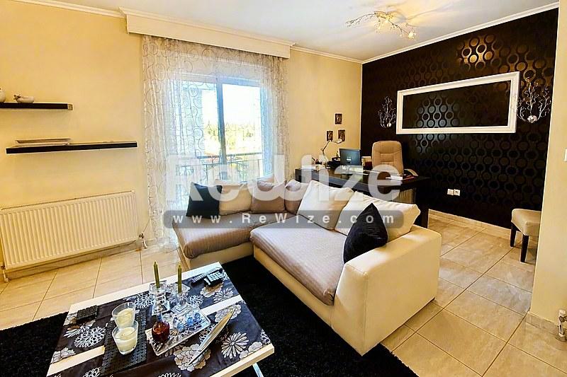 Κομψό σαλόνι μεζονέτας στη Χαλκιδική με κρεμ γωνιακό καναπέ, σκούρο τοίχο και σύγχρονη διακόσμηση.