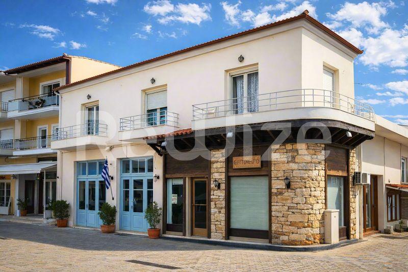 Σύγχρονη πρόσοψη μονοκατοικίας στη Χαλκιδική με πέτρινη και κρεμ εξωτερική επένδυση, μπλε παράθυρα και εμπορικό χώρο στο ισόγειο.