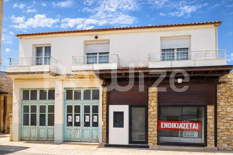 Πρόσοψη μονοκατοικίας στη Χαλκιδική με διώροφη λευκή και τοιχοποιία κόκκινου χρώματος, πράσινα παράθυρα και χώρο καταστήματος.