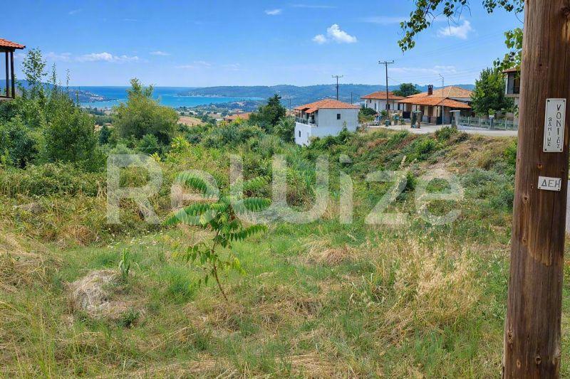 Οικόπεδο στην Χαλκιδική με θέα στη θάλασσα, πράσινη βλάστηση και κατασκευές στην περιοχή.
