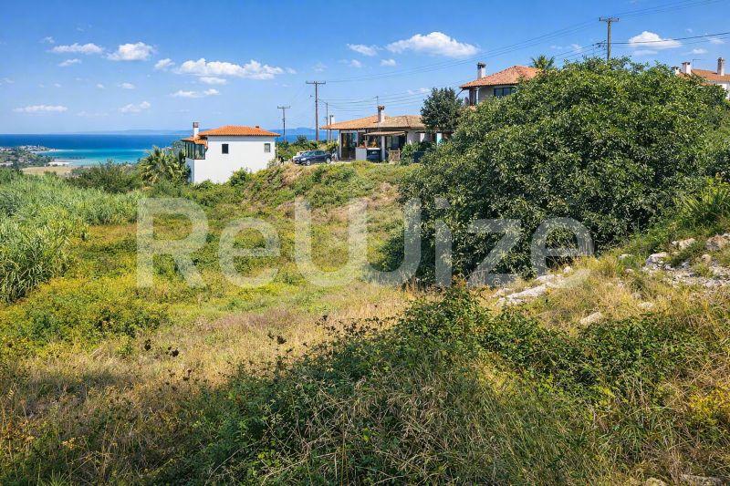 Οικόπεδο στη Χαλκιδική με θέα στη θάλασσα, μεσογειακή βλάστηση και παραδοσιακές κατοικίες.