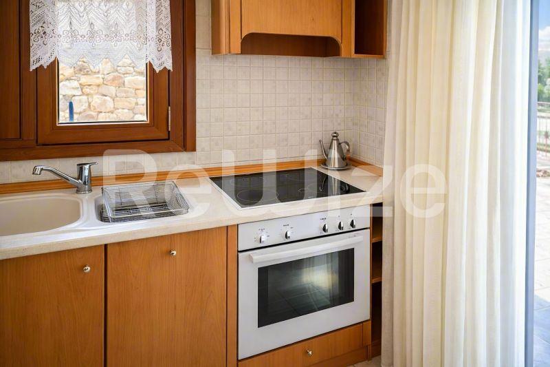 Συμπαγής κουζίνα μεζονέτας στη Χαλκιδική με ξύλινα ντουλάπια, λευκές επιφάνειες και σύγχρονες συσκευές.