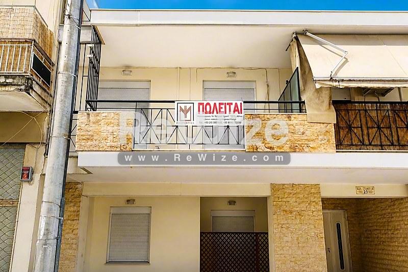 Πρόσοψη διαμερίσματος στη Χαλκιδική με κίτρινη πέτρα και μπαλκόνια, με πινακίδα ενοικίασης.
