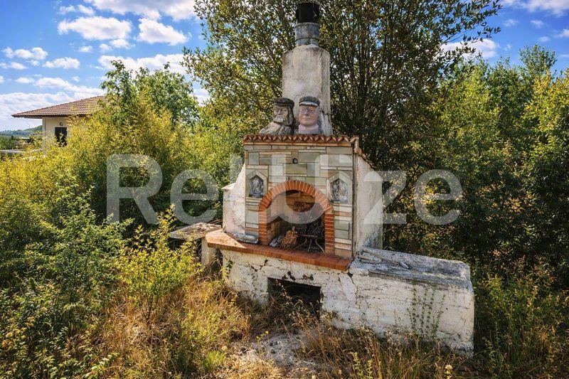 Παραδοσιακό πετρόχτιστο μπάρμπεκιου με καπνοδόχο σε μονοκατοικία στη Χαλκιδική, περιτριγυρισμένο από πράσινο.