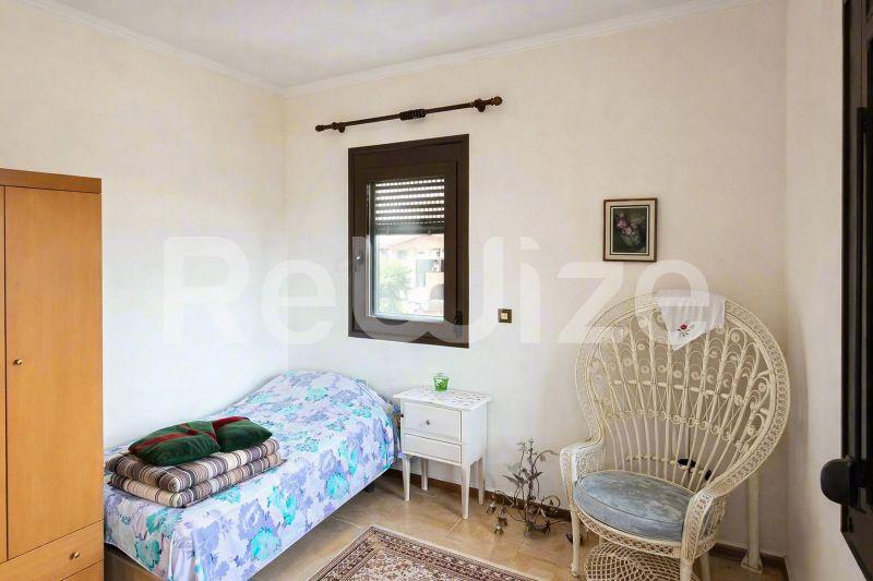 Φωτεινό υπνοδωμάτιο σε μονοκατοικία στη Χαλκιδική με κρεβάτι, καρέκλα και παράθυρο με παντζούρια.