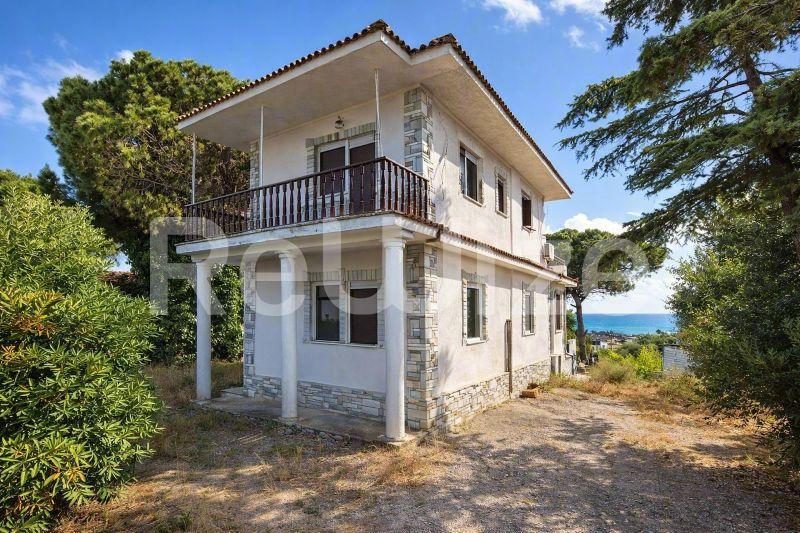 Γοητευτική πρόσοψη μονοκατοικίας στη Χαλκιδική με λευκά τοιχώματα, ξύλινα παντζούρια και θέα στη θάλασσα.