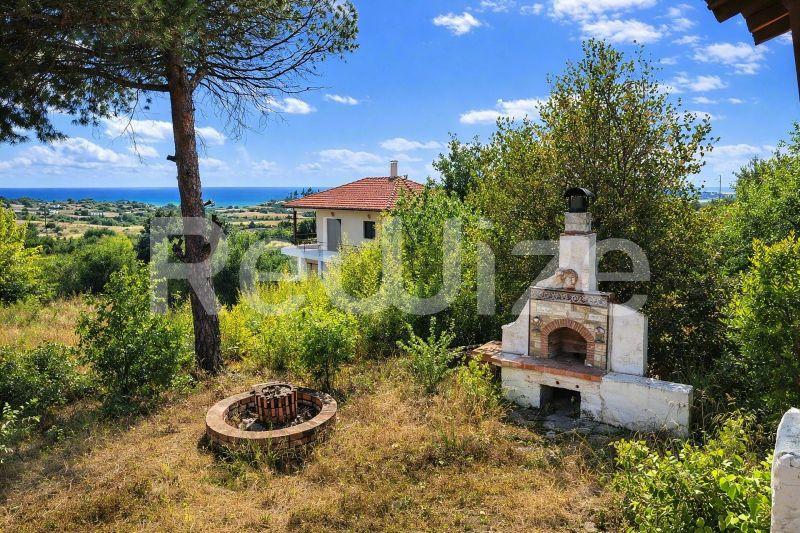 Ευρύχωρος κήπος μονοκατοικίας στη Χαλκιδική με δέντρα, παραδοσιακό τζάκι και θέα στη θάλασσα.