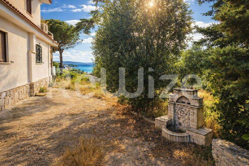 Κήπος μονοκατοικίας στη Χαλκιδική με θέα στη θάλασσα, με ώριμα δέντρα και παραδοσιακή πέτρινη κατασκευή.