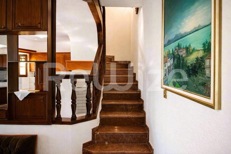 Ξύλινη σκάλα σε μονοκατοικία στη Χαλκιδική, που οδηγεί στον επάνω όροφο με λευκή σχάρα πετσετών και τοπίο.