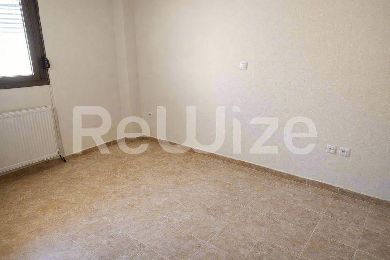 Просторна κρεβατοκάμαρα σε μεζονέτα στη Χαλκιδική με πλακόστρωτο δάπεδο και φυσικό φως από το παράθυρο.