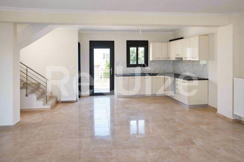 Σύγχρονη κουζίνα με λευκά ντουλάπια σε μεζονέτα της Χαλκιδικής, με μαύρες επιφάνειες και πρόσβαση στον κήπο.