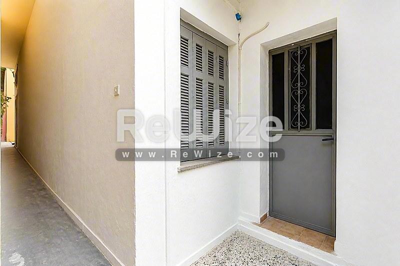 Καθαρή είσοδος διαμερίσματος στη Χαλκιδική με γκρίζια πόρτα, περσίδες και πλακόστρωτο πάτωμα.