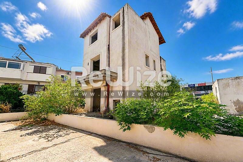 Πρόσοψη μονοκατοικίας στη Χαλκιδική με διώροφη κατασκευή από σκυρόδεμα και περιβάλλουσα πράσινη βλάστηση.
