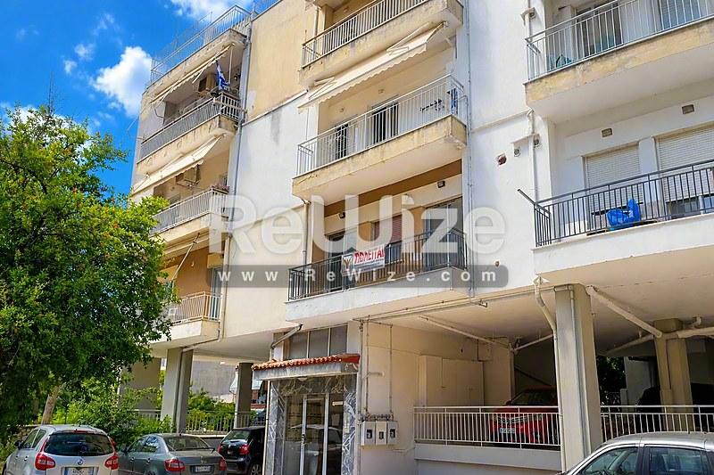 Πρόσοψη διαμερίσματος στη Χαλκιδική με πολυώροφη οικοδομή, μπαλκόνια και εμπορικό χώρο στο ισόγειο.