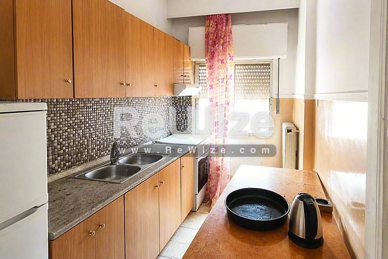 Συμπαγή κουζίνα διαμερίσματος στη Χαλκιδική με ξύλινα ντουλάπια, πλακάκια μωσαϊκού και σύγχρονες συσκευές.