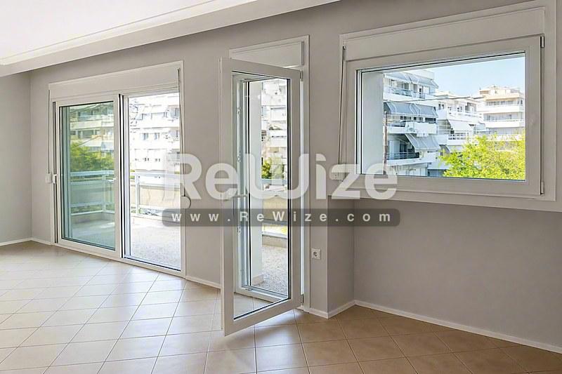 Φωτεινό σαλόνι διαμερίσματος στη Χαλκιδική με σύγχρονες γυάλινες πόρτες, μεγάλα παράθυρα και πρόσβαση σε ιδιωτικό μπαλκόνι.