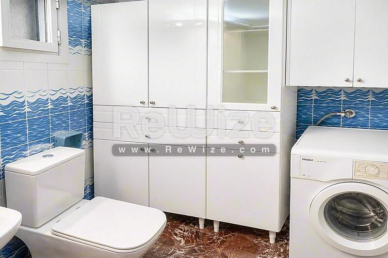 Σύγχρονο μπάνιο διαμερίσματος στη Χαλκιδική με λευκά ντουλάπια, μπλε πλακάκια κύματος και πλυντήριο ρούχων.