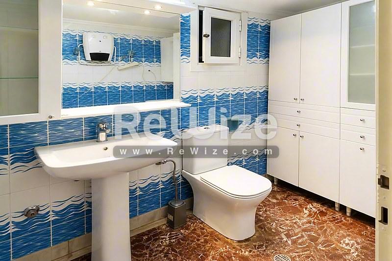 Σύγχρονο μπάνιο διαμερίσματος στη Χαλκιδική με μπλε πλακάκια, νιπτήρα και λευκά ντουλάπια.