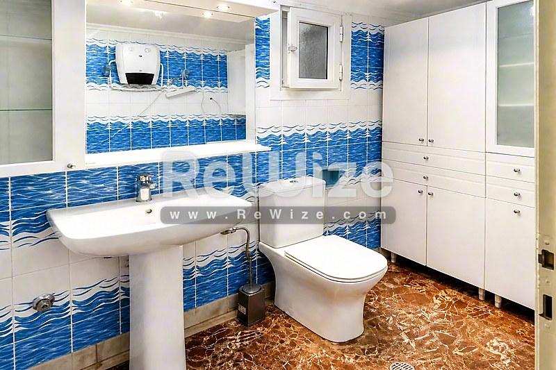 Σύγχρονο μπάνιο διαμερίσματος στη Χαλκιδική με μπλε πλακάκια μωσαϊκού, νιπτήρα, λεκάνη και λευκές ντουλάπες.