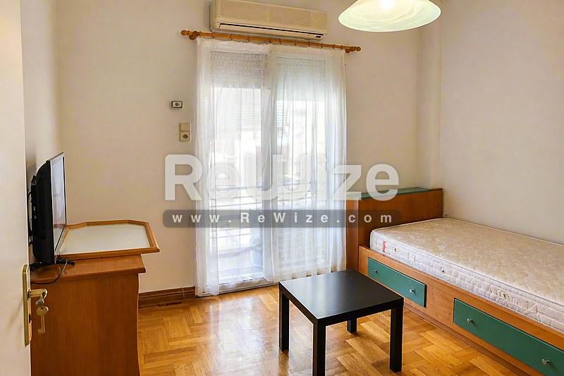 Φωτεινό υπνοδωμάτιο διαμερίσματος στη Χαλκιδική με μονό κρεβάτι, ξύλινο γραφείο και γυάλινες πόρτες με θέα.