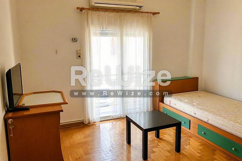 Φωτεινό υπνοδωμάτιο διαμερίσματος στη Χαλκιδική με ξύλινο κρεβάτι, γραφείο και πρόσβαση σε μπαλκόνι.