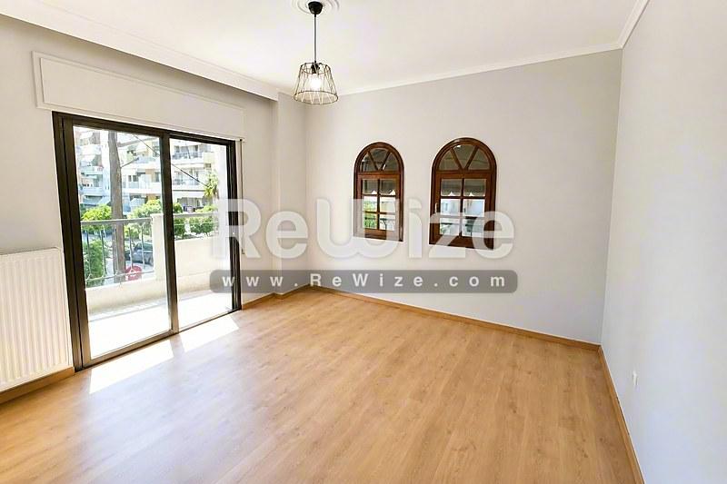 Φωτεινό σαλόνι διαμερίσματος στην Χαλκιδική με ξύλινα δάπεδα, μεγάλες γυάλινες πόρτες και διακοσμητικά τοξωτά παράθυρα.