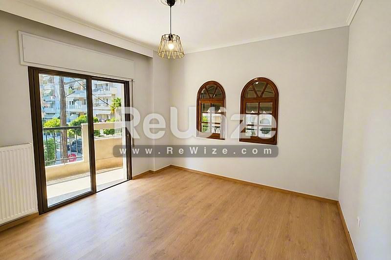 Φωτεινό σαλόνι διαμερίσματος στη Χαλκιδική με ξύλινο πάτωμα, γυάλινες πόρτες μπαλκονιού και διακοσμητικούς ξύλινους καθρέφτες.