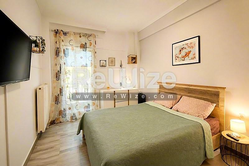 Άνετο υπνοδωμάτιο σε διαμέρισμα της Χαλκιδικής με ξύλινο κρεβάτι, πράσινη κάλυψη και φυσικό φως από την πόρτα του μπαλκονιού.