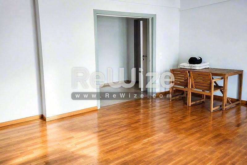 Ευρύχωρο σαλόνι με ξύλινο δάπεδο στην ιδιότητα Halkidiki rw-7434, με minimal έπιπλα και μοντέρνες γυάλινες πόρτες.