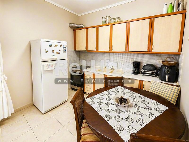 Συμπαγή κουζίνα με ξύλινα έπιπλα στο ακίνητο Halkidiki rw-7479, με τραπέζι φαγητού και βασικές συσκευές.