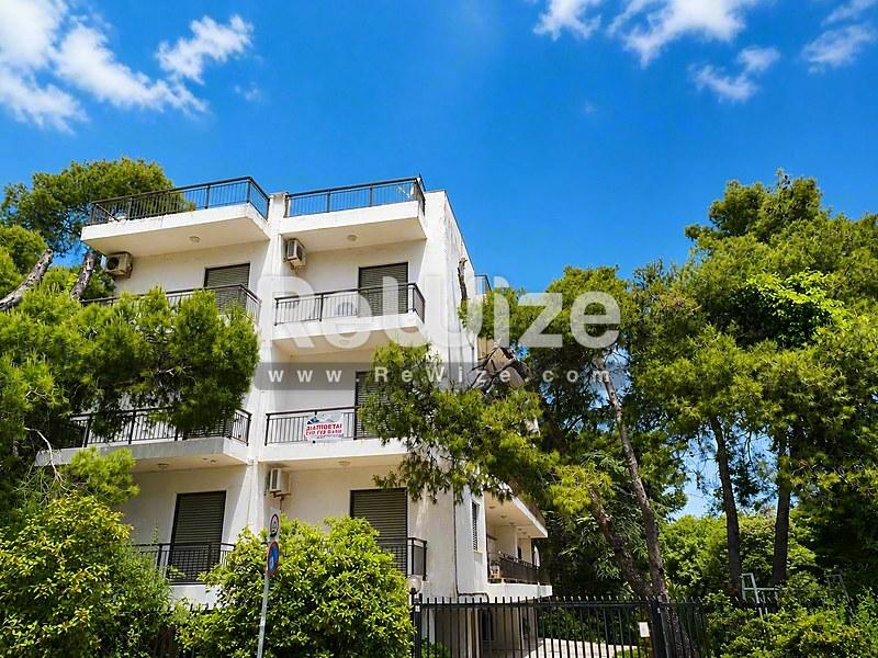 Σύγχρονο λευκό κτίριο διαμερισμάτων περιτριγυρισμένο από πολλά πράσινα δέντρα στη Χαλκιδική.