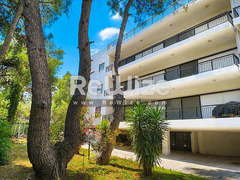 Σύγχρονο κτίριο διαμερισμάτων στη Χαλκιδική με μπαλκόνια, περιτριγυρισμένο από ψηλά πεύκα και τροπικά φυτά.