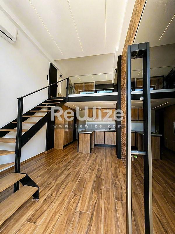 Ανοιχτό loft στη Χαλκιδική με ξύλινα πατώματα, υπνοδωμάτιο σε μεσογείωση και σύγχρονες μαύρες μεταλλικές κάγκελα.