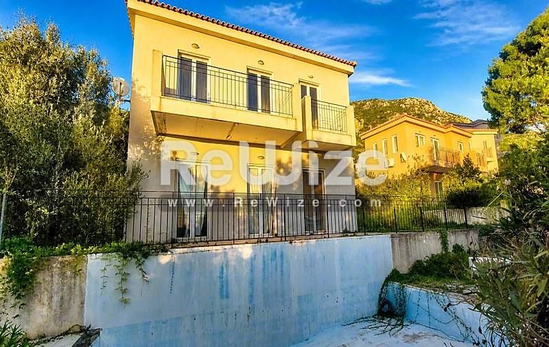Κίτρινη διώροφη βίλα στη Χαλκιδική με γαλάζια πύλη και μεσογειακό τοπίασμα.
