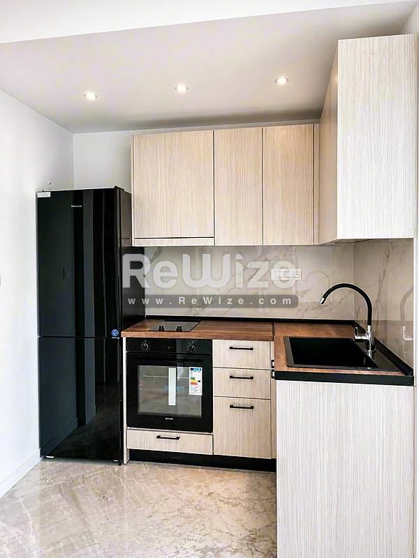 Σύγχρονη κουζίνα στο κτίριο rw-7710 Χαλκιδικής με ανοιχτά ξύλινα έπιπλα, μαύρες συσκευές και μαρμάρινες επιφάνειες.