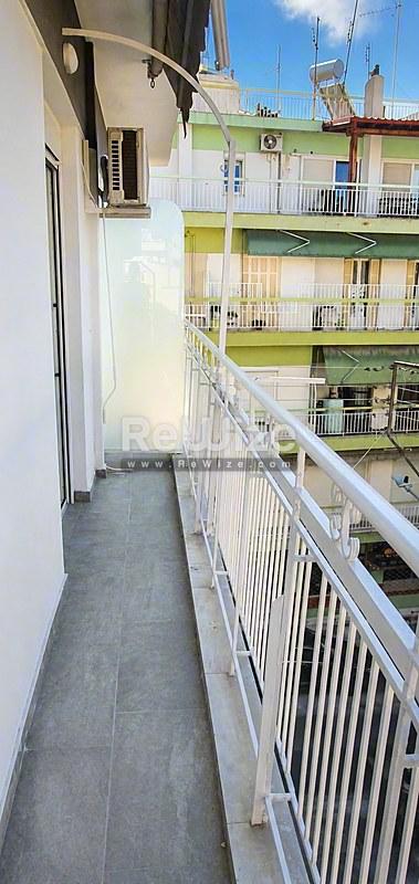 Στενό μπαλκόνι του διαμερίσματος rw-7713 στη Χαλκιδική με λευκές κάγγελες και θέα στα γειτονικά κτίρια.