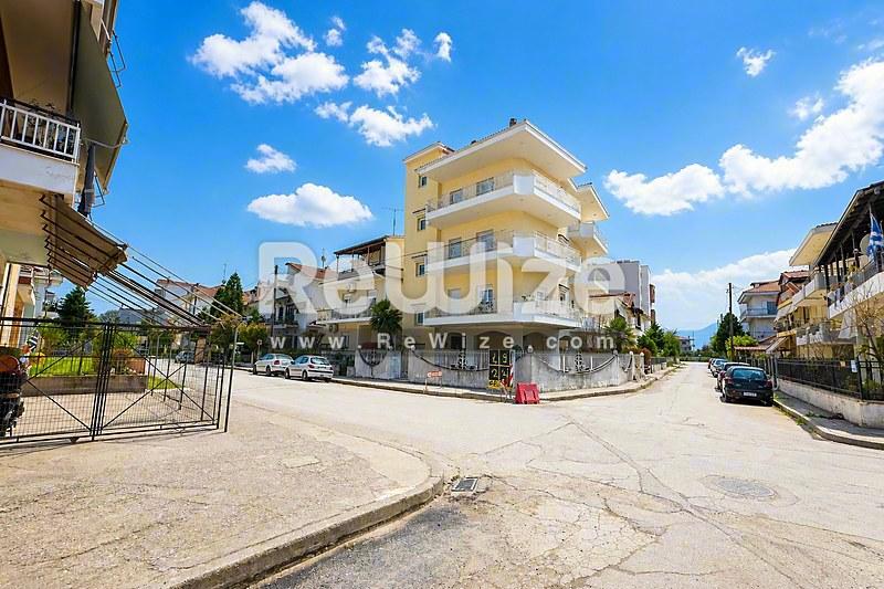 Κίτρινη πρόσοψη διαμερίσματος στη Χαλκιδική με μπαλκόνια που βλέπουν σε ηλιόλουστο οικιστικό δρόμο.