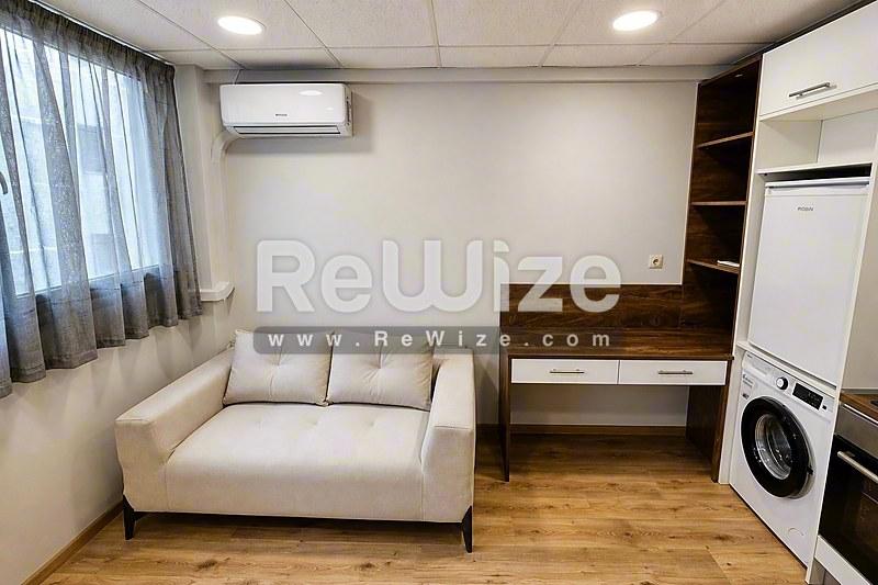 Σύγχρονο σαλόνι διαμερίσματος στη Χαλκιδική με άνετο μπεζ καναπέ, ξύλινο γραφείο και ενσωματωμένο πλυντήριο.