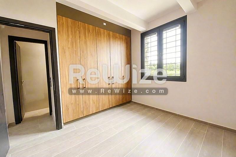 Φωτεινό υπνοδωμάτιο σε διαμέρισμα της Χαλκιδικής με ξύλινες ντουλάπες, ανοιχτό δάπεδο και παράθυρο με παντζούρια.