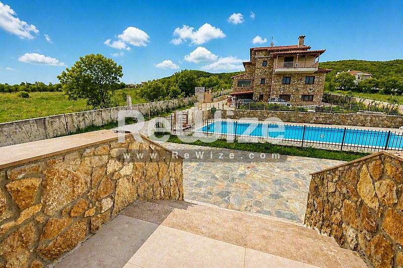 Πισίνα διαμερίσματος στη Χαλκιδική με πέτρινη βίλα και περιποιημένους χώρους κάτω από γαλάζιο ουρανό.
