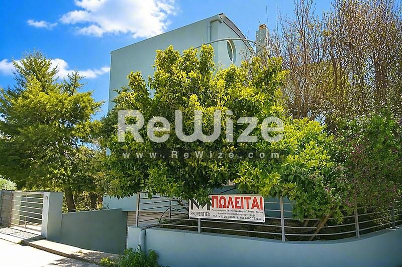 Σύγχρονη πρόσοψη μονοκατοικίας στη Χαλκιδική με πλούσια πράσινη βλάστηση και σχεδιασμό.