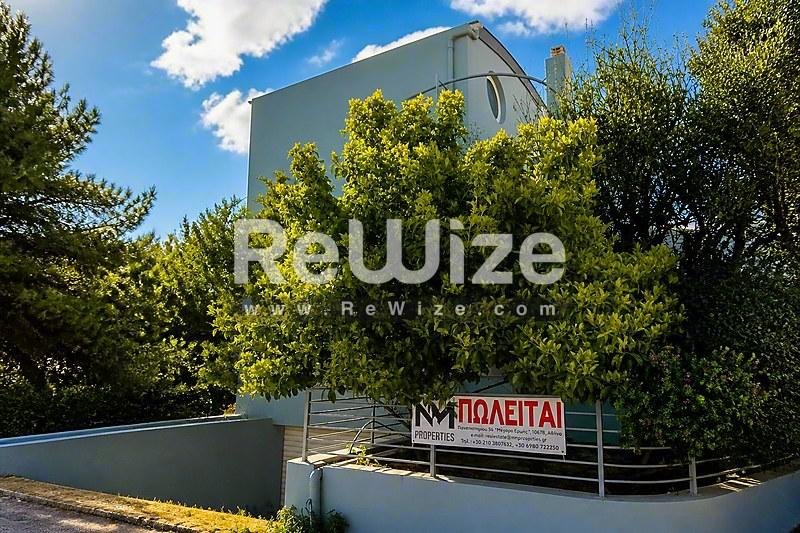 Σύγχρονη όψη μονοκατοικίας με πλούσια πράσινη βλάστηση στην Χαλκιδική, διακρινόμενη από σύγχρονη αρχιτεκτονική.