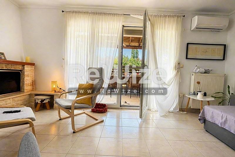 Φωτεινό σαλόνι μεζονέτας στη Χαλκιδική με σύγχρονα έπιπλα, τζάκι και γυάλινες πόρτες προς τη βεράντα.